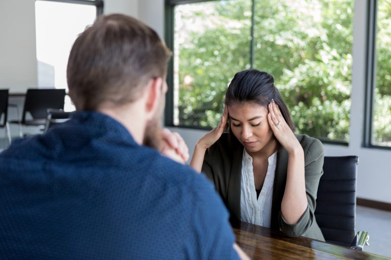 An upset woman, with her head in her hands, discusses issues with an attentive male counselor.