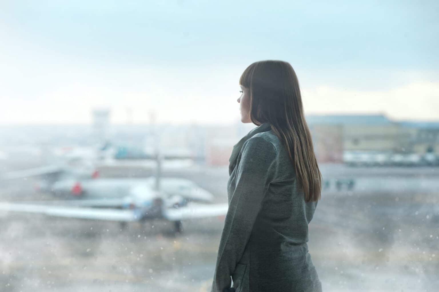 Woman standing outside an airport looking at a plane.