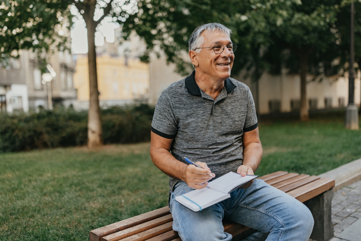 Happy man sitting on a bench working on his 2025 resolutions.